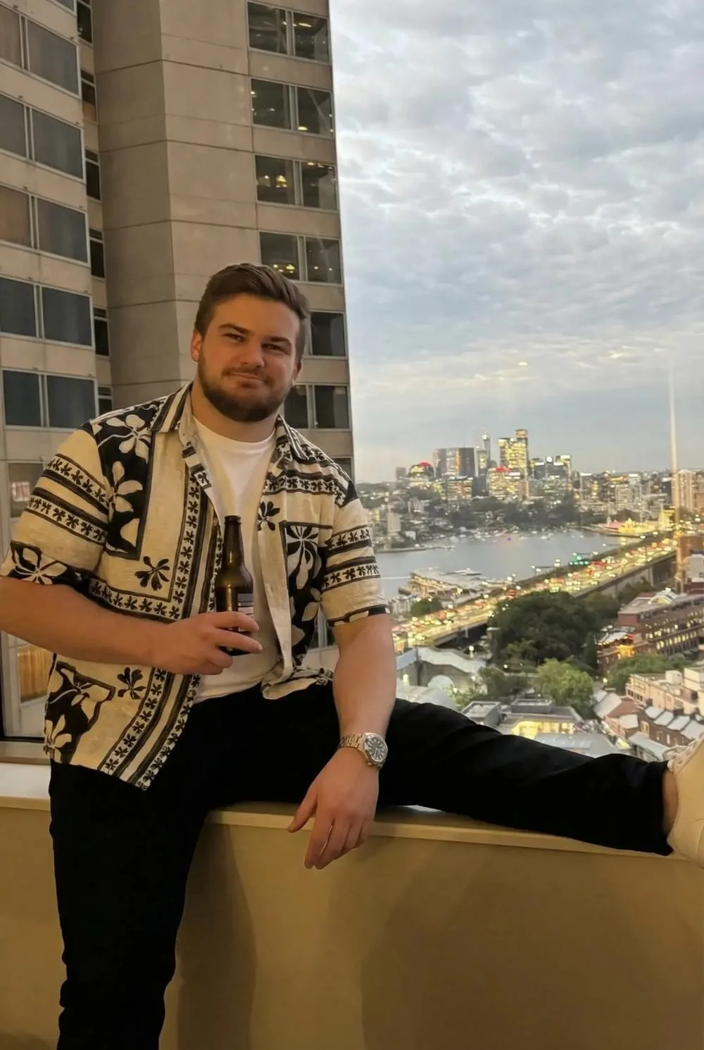 Ben sitting on a rooftop ledge, the Sydney skyline behind him