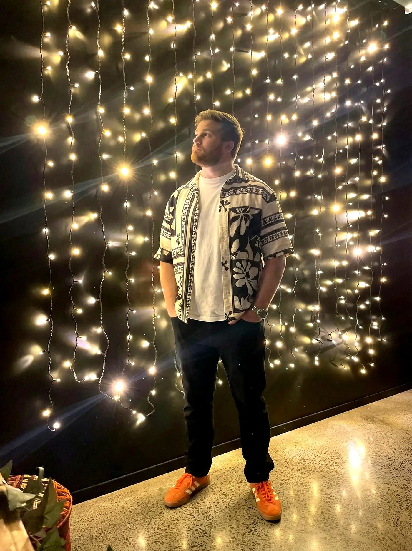 Ben in front of a wall of fairy lights, hands in pockets
